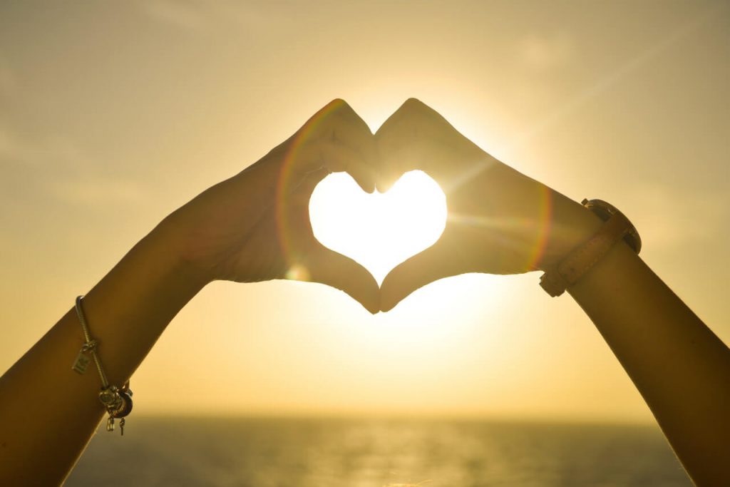 coeur formé avec deux main devant couché de soleil