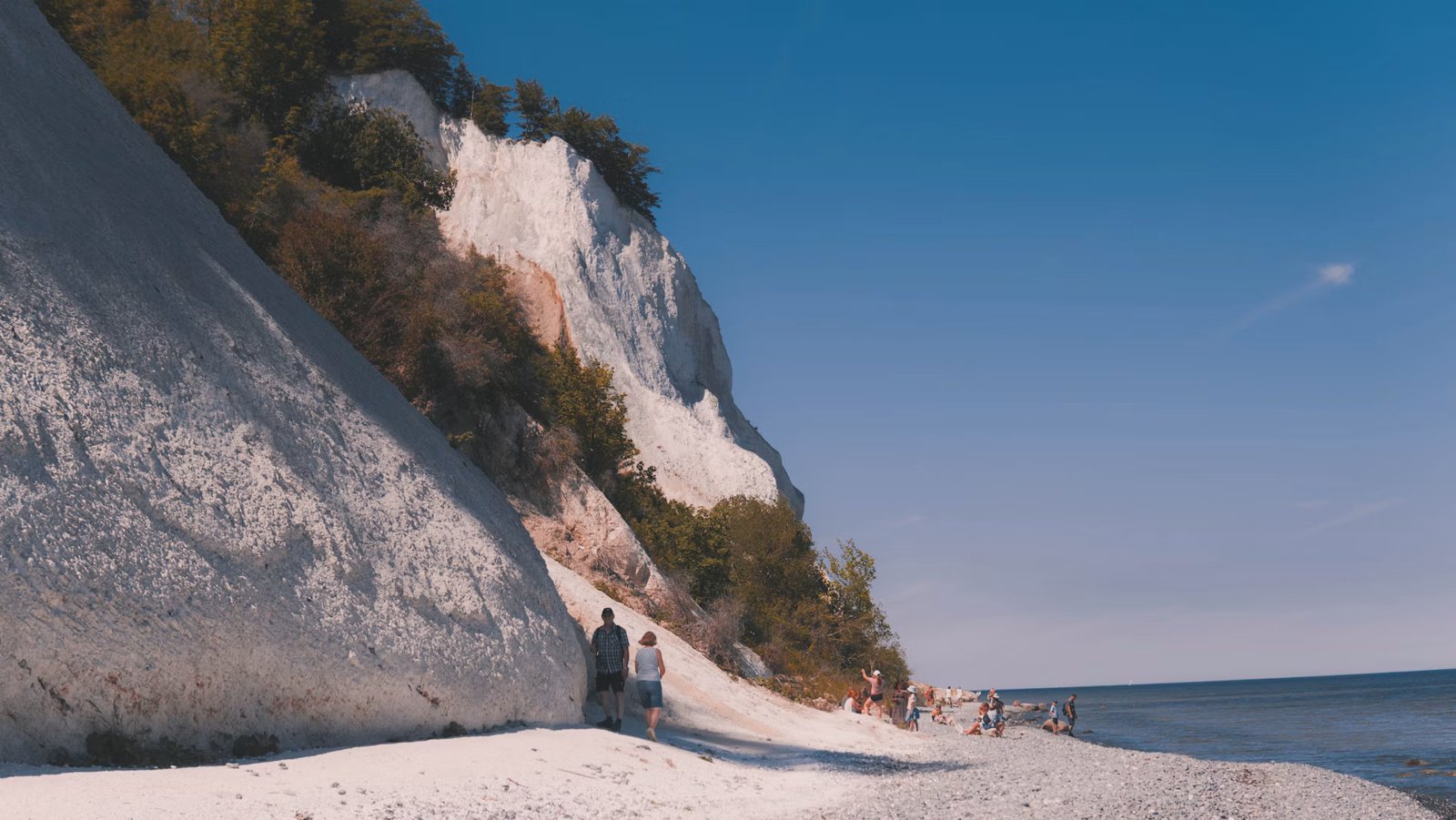 Des promeneurs marchent sur une plage au pied de falaises blanches.