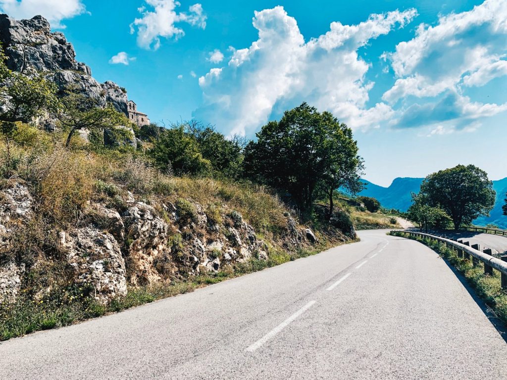Une route sinueuse longe le flanc d'une montagne rocheuse sous un ciel bleu.