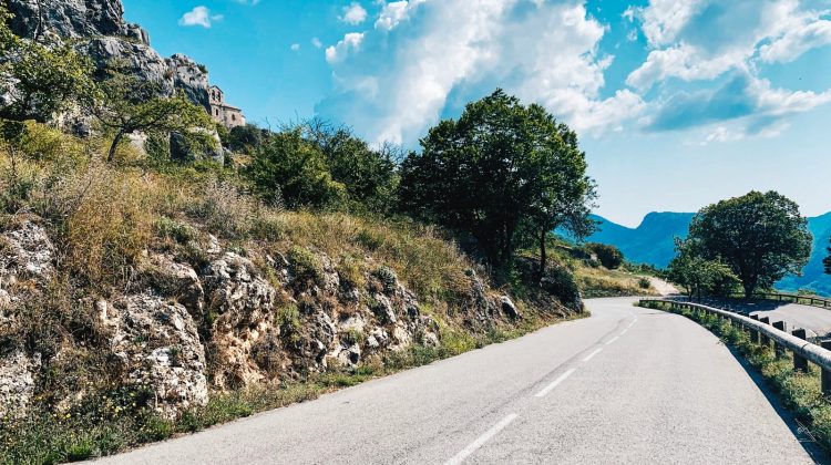 Une route sinueuse longe le flanc d'une montagne rocheuse sous un ciel bleu.